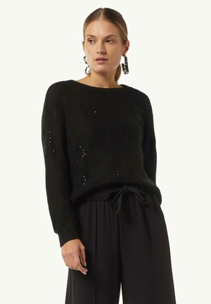 Schwarzer Strickpullover mit lässiger Passform, verziert mit subtilen Pailletten, Rundhalsausschnitt und langen Ärmeln. Kombiniert mit weit geschnittenen schwarzen Hosen.