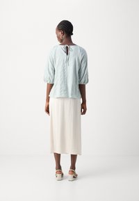 Lys blå, teksturert bluse med puffede ermer og båndlukking på ryggen, kombinert med en kremfarget, ankellang skjørt og beige hælsandaler.