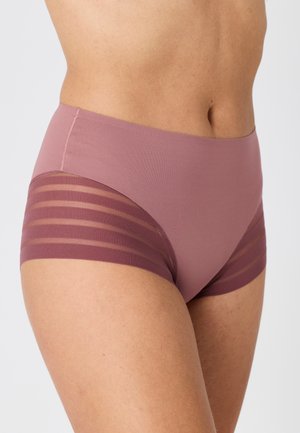 Mujer con ropa interior de talle alto en color malva con líneas horizontales transparentes en los paneles de la cadera sobre un fondo liso y claro.