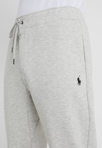 Vaaleanharmaat pehmeästä kankaasta valmistetut collegehousut, joissa on joustava vyötärö, säädettävä nyöri ja pieni musta logo vasemmassa lahkeessa.