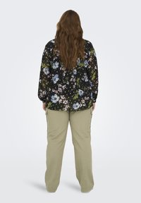 Blusa nera floreale con maniche lunghe, decorata con fiori blu e rosa. Abbinata a pantaloni cargo verde chiaro con tasche laterali e una vestibilità morbida.