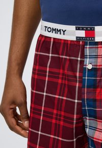 Καρό ανδρικά μποξεράκια με συνδυασμό κόκκινου και μπλε χρώματος, διαθέτοντας ελαστική ζώνη μέσης σε λευκό με το λογότυπο TOMMY HILFIGER και λεπτομέρεια με κουμπί.