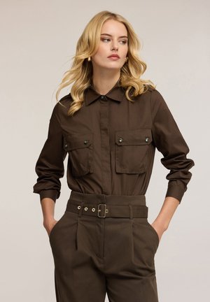 Brązowa koszula z kołnierzykiem, z dwoma kieszeniami na piersi i zapięciem na zatrzaski, w połączeniu z brązowymi spodniami o wysokim stanie z paskiem w talii.