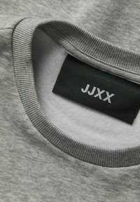 Felpa grigia con scollo rotondo. Il tessuto è morbido e strutturato, con un'etichetta nera che riporta la scritta "JJXX" in lettere bianche.