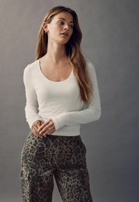 Hvid langærmet top med en scoop-udskæring, parret med olivenbrune leopardmønstrede bukser, der har en løs pasform og sidelommer.