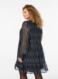 Musta mekko, jossa on läpikuultavat pitkät hihat ja hopeiset pystysuorat raidat. Mekossa on röyhelöhelma ja rento istuvuus, joka korostaa tekstuurillista muotoilua.