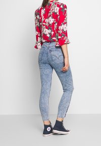 Red floral blouse with ruffled sleeves paired with light blue skinny jeans featuring a faded texture and side stripe detail. Blue canvas sneakers.