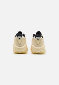 Sneakers med en beige ruskindsoverdel, sorte mesh-detaljer og en gummisål med hexagonale designmønstre. Fresh foam-branding synlig.
