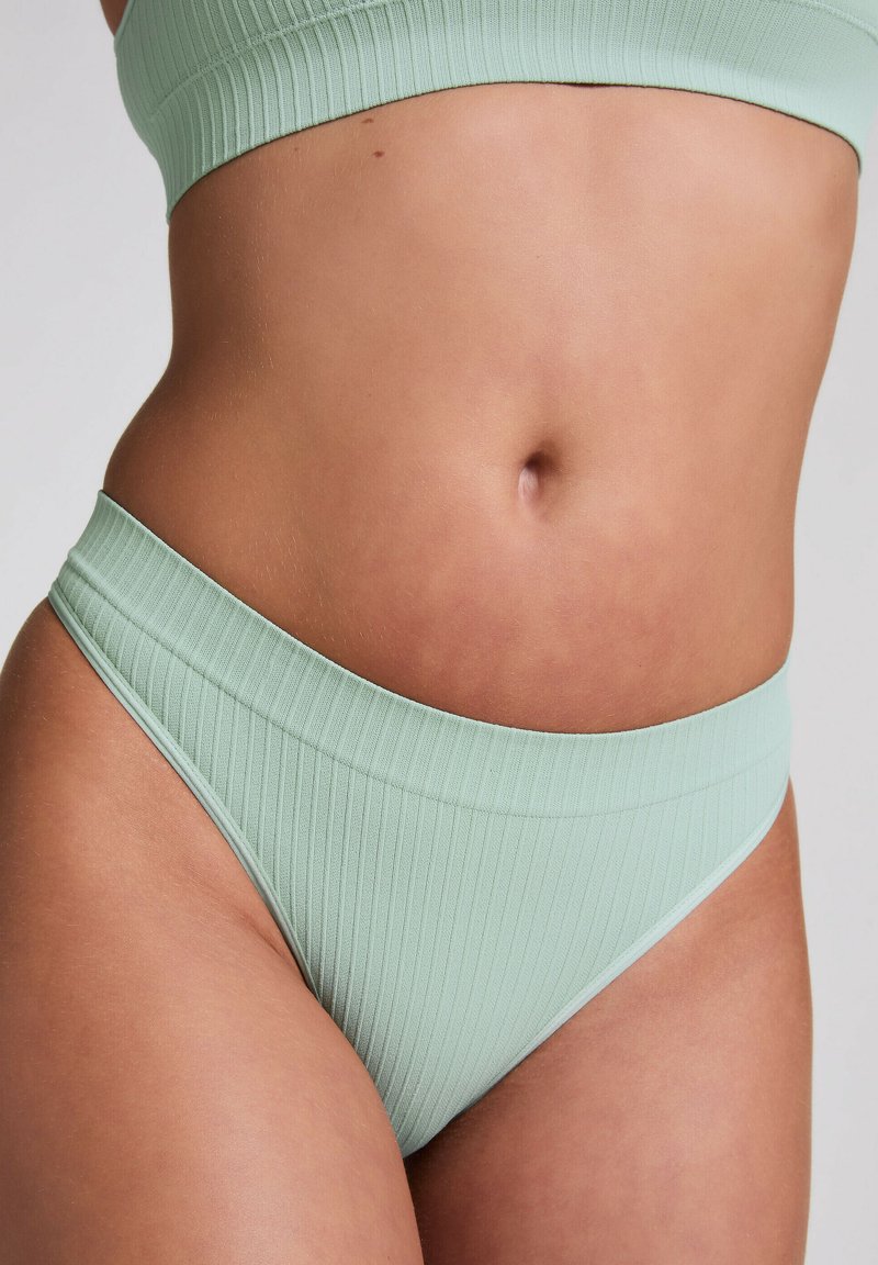 Hellgrüner, gerippter Bikini-Unterteil mit breitem Bund, nahtlosen Kanten und einem schlichten, modernen Schnitt. Weiche Textur, die für Komfort steht.
