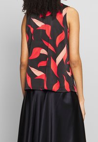 Personne portant un haut sans manches noir avec des motifs de feuilles rouges et roses et une jupe noire brillante, vue de dos.