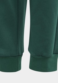 Puños de sudadera verde con textura acanalada, dobladillo elástico y tejido suave. Presenta un detalle de costura a lo largo del lado exterior.