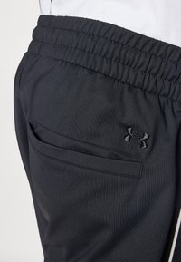 Svarta sportshorts i mjukt tyg, med elastisk midja, en sydd ficka och en liten logotyp nära midjan.