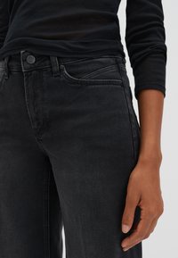 Black denim jeans with a straight leg design, button closure, and side pockets; fabric has a smooth texture with a slight sheen.