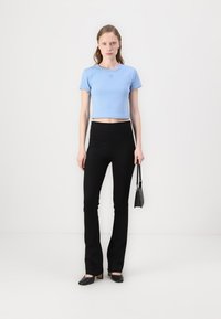 Tricou scurt de culoare albastru deschis, cu mâneci scurte, combinat cu pantaloni negri evazați cu talie înaltă și tocuri negre cu vârful ascuțit.