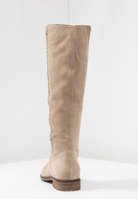 Botte haute jusqu'au genou en daim beige avec un talon en bois plat, comprenant un détail de couture latérale texturée et un design à bout arrondi.