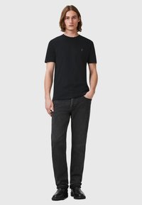 T-shirt nera con scollatura rotonda, maniche corte e un logo sottile sul petto, abbinata a jeans scuri e stivali neri.