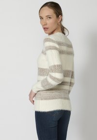 Soehka triibuline sveter kreemi ja pruuni tooni. Omab pikki varrukaid, ümmargust kaelust ja tekstureeritud kudumismustrit. Koos tumedate teksadega.