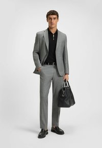 Szary garnitur w wzory z klapami, czarna koszulka polo, czarny pasek i fakturowana czarna torba na ramię. Czarne mokasyny dopełniają stylizację.