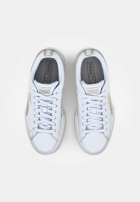 Weiße Sportsneakers mit einem glatten Lederobermaterial, flachen Schnürsenkeln und goldenen Akzenten. Sie verfügen über eine gepolsterte Sohle und ein Logo auf der Zunge.