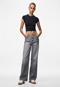 Melna pieguļoša t-krekls, kas kombinēts ar pelēkiem platām kājām džinsiem. Džinsiem ir augsta josta, redzams šuvums un priekšējie kabatas. Izskatu papildina ikdienišķi sporta apavi.