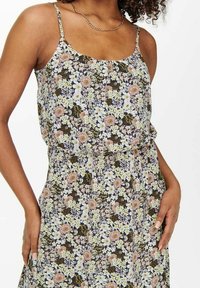 Ärmelloses Blumenkleid mit einer Mischung aus rosa, gelben und weißen Blumen auf einem dunklen Hintergrund, mit tailliertem Schnitt und weichem Stoff.