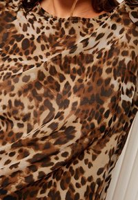 Tissu à imprimé léopard dans des tons de brun et beige, présentant une texture lisse et soyeuse avec des taches de différentes tailles et un style drapé.