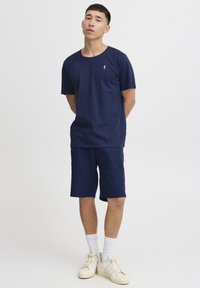 Mørkeblå T-shirt med korte ærmer og et lille isvaffel-logo. Matchet med mørkeblå shorts. Hvide sportsko og ankelsokker.