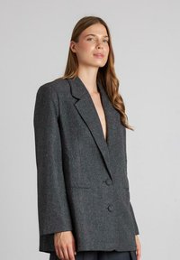 Grijze gestructureerde blazer met een reverskraag, dubbele knopen en een textiel met subtiele patronen en zijzakken.