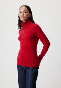 Maglione a collo alto lavorato a maglia rossa con mezzi zip, polsini e orlo a coste. Abbinato a pantaloni in denim blu scuro, dal fit slim.