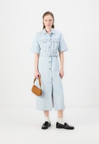 Lyseblå denimskjortekjole med korte ermer, belted midje, frontknapper og knelengde. Kombinert med en brun veske og svarte sko.