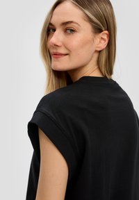 Zwarte katoenen T-shirt met opgerolde mouwen, met een ontspannen pasvorm en een zachte textuur; gezien vanaf de zijkant met een zachte halslijn.