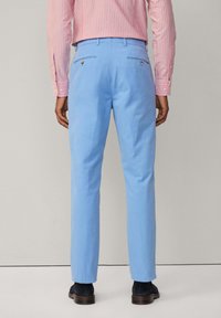 Pantalons bleu clair en toile de coton, présentant une coupe slim, des accents de poches arrière et une finition lisse, assortis à une chemise rayée rose.