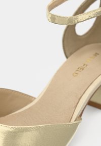 Guldmetalliska högklackade sandaler med en tunn vristrem, en slät texturerad innersula och en strukturerad häl med en subtil kurva.
