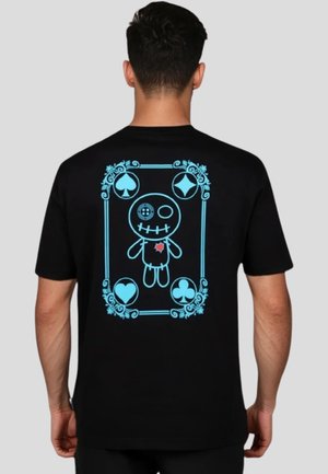 Camiseta negra con un gráfico azul de una muñeca de trapo rodeada de símbolos de cartas y acentos florales en la parte de atrás.