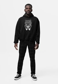 Sudadera negra con estampado gráfico blanco que presenta guitarras y un emblema. Combinada con pantalones de cuadros negros y zapatillas negras.