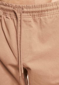 Beige joggerpants met een elastische tailleband, zichtbare stiksels en een gladde katoenen textuur met een losse pasvorm.