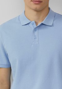Svetlo modra polo majica z klasičnim ovratnikom, trojnim gumbom in mehko, teksturirano tkanino z rahlo raztegljivostjo.