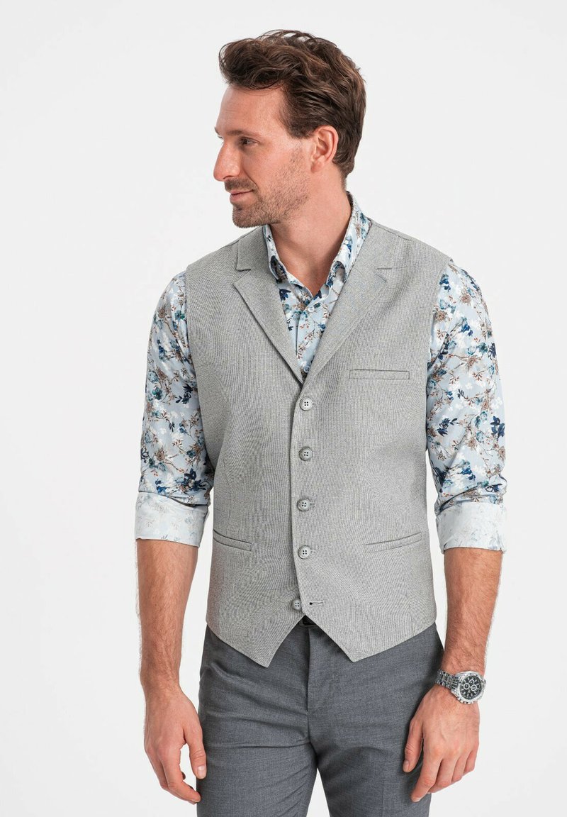 Grijze textuur vest met vijf knopen, gecombineerd met een bloempatronen shirt. Model draagt grijze broeken en een horloge. Zijkant profielweergave.