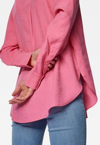 Camicia di lino rosa chiaro con un fit rilassato, polsini con bottoni e orlo curvo. Le cuciture a vista e le fessure laterali accentuano il design.