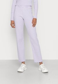Calças listradas em roxo e branco com um corte solto, apresentando uma bainha desfiada e combinadas com ténis atléticos brancos.