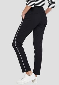 Mustat housut, joissa on kapea malli, valkoiset sivuraidat sekä etu- ja takataskut. Yhdistetty raidalliseen yläosaan ja valkoisiin tennareihin.