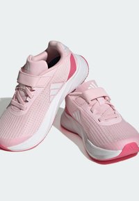 Scarpe sportive rosa con tomaia in rete traspirante, cinturino in Velcro e dettagli bianchi. Presentano una punta arrotondata e una suola imbottita.