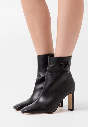 Black leather ankle boot with a sleek design, pointed toe, and a high stiletto heel. Features a small logo accent on the side.