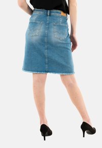 Falda de mezclilla en azul claro, de longitud media con dobladillo deshilachado, que presenta dos bolsillos traseros con detalles de costura curva. Combinada con tacones altos negros.