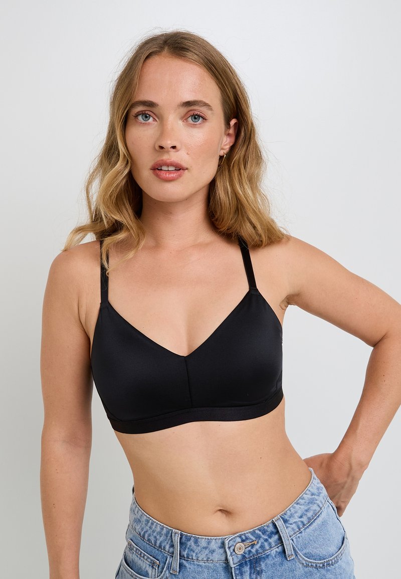 Bralette nera con una texture liscia e lucida, scollatura a V, spalline regolabili e una fascia solida nella parte inferiore, abbinata a pantaloni shorts in denim a vita alta.