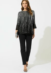 Top nero con paillettes e linee verticali, maniche a tre quarti; abbinato a pantaloni neri e scarpe con cinturino. Borsa a mano argentata in una mano.