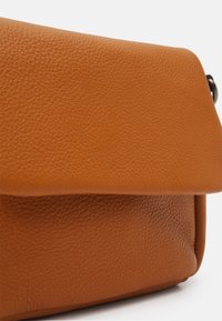 Hnědá kožená crossbody taška s texturou, se skládacím víkem a viditelnou kovovou sponou na boku na bílém pozadí.