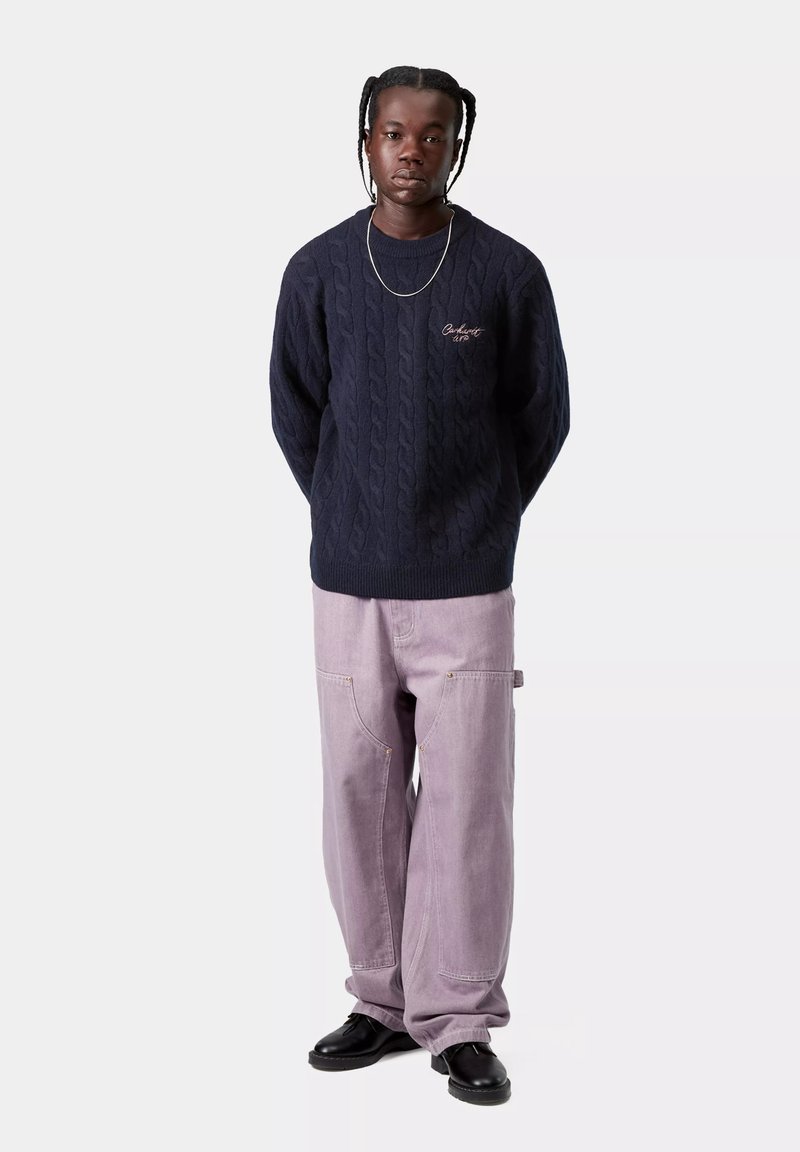 Maglione blu navy a trecce con polsini e orlo a coste, abbinato a pantaloni larghi viola chiaro con tasche e dettagli in oro. Scarpe nere.