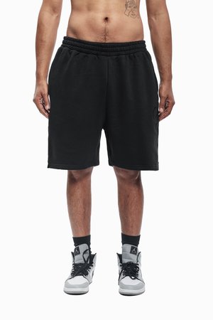 Czarne bawełniane krótkie spodnie dresowe z elastycznym pasem, sięgające do kolan, z bocznymi kieszeniami, zestawione z czarno-białymi wysokimi trampkami.