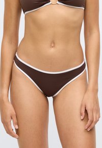 Rudos bikini apatiniai su baltais kraštais, su briaunotu paviršiumi ir žemu juosmeniu. Tinka maudymosi kostiumams arba paplūdimio aprangai.